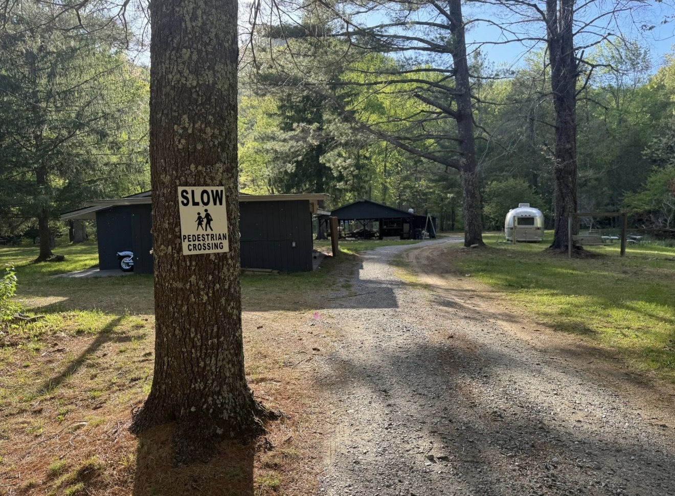Gravel driveway with Airstream and wooded entrance to the property