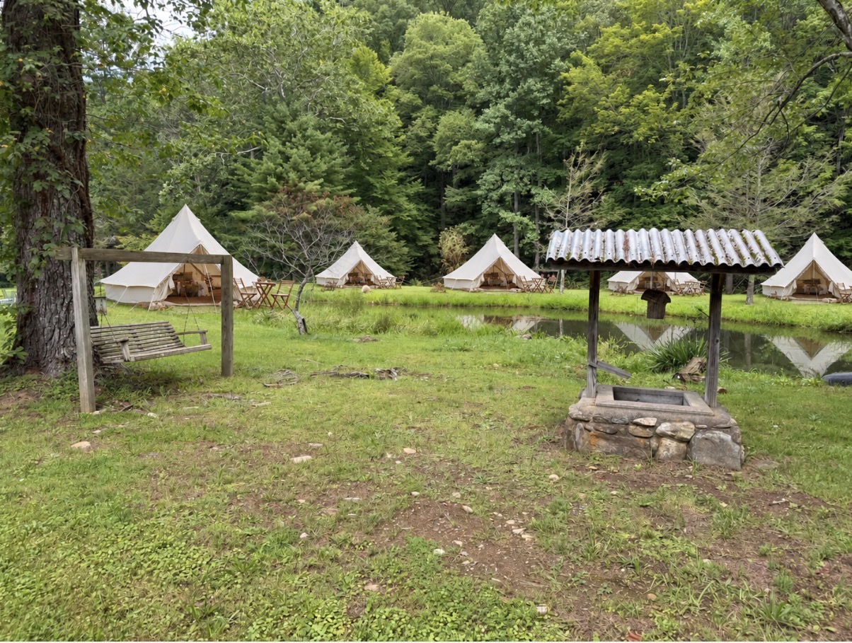 Five cream canvas glamping bell tents arranged around the pond at Bluehead Waters